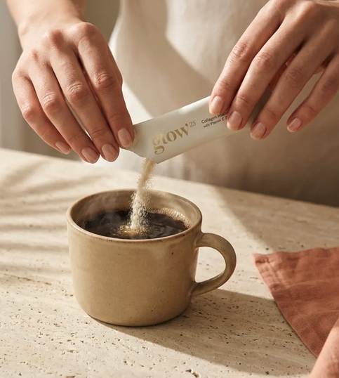 Frauenhände schütten Pulver aus einem Glow25-Sachet in eine Steingut-Kaffeetasse; Text "glow25" und 
